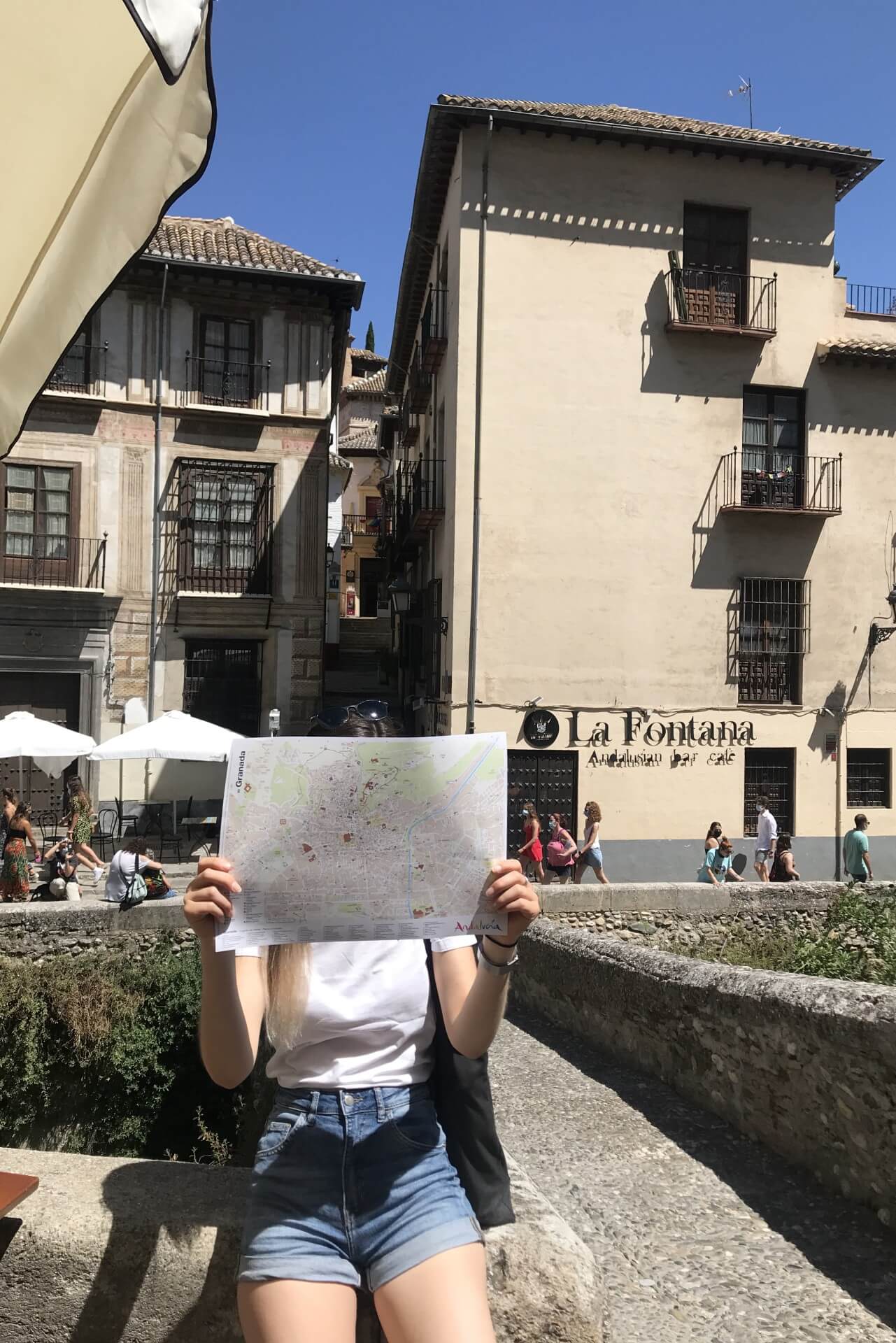 natali sitting on a small wall holding a map of granada in front of her face
