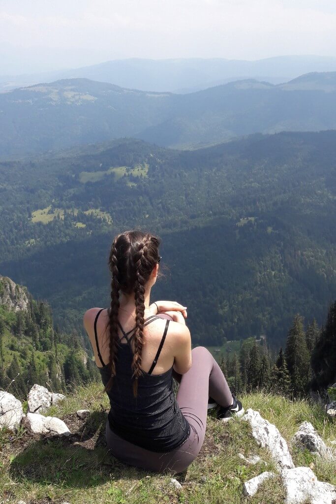 girl with double dutch braids hairstyle backpacking, sitting in the mountains looking at the landscape