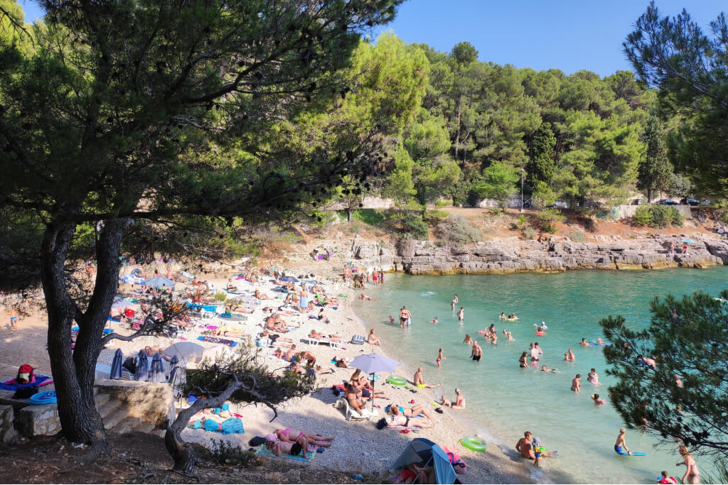 a cove in pula with a pebbled beach and turqouise sea with people on the beach and swimming in the water