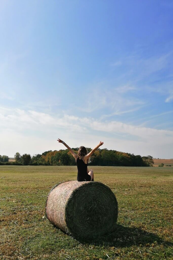 girl sitting on a ball of hay on a clear summer day 