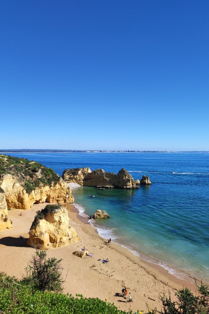 a sandy beach surrounded by steep cliffs on a clear blue day with bright blue sea in lagos algarve