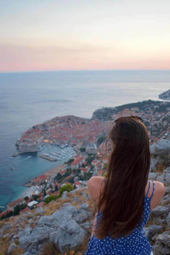 girl with brown hair facing away from the camera overlooking the sunset over dubrovnik from srd mountain