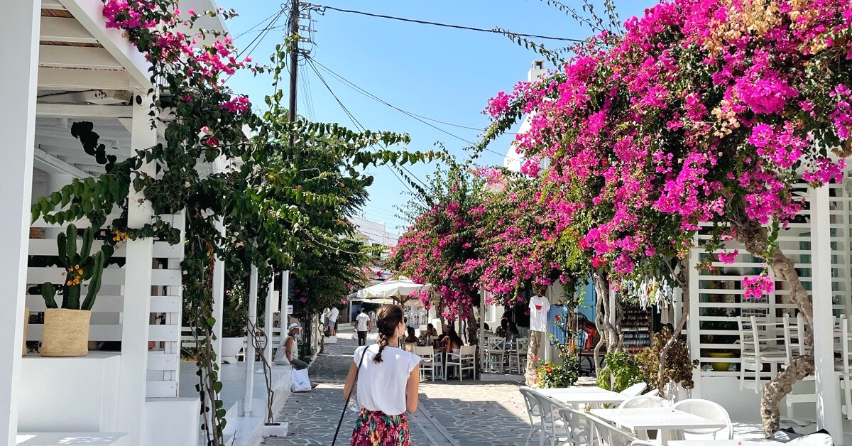 girl walking the cobblestone streets of antiparos surrounded by pink trees and picturesque cafes on a day trip from paros