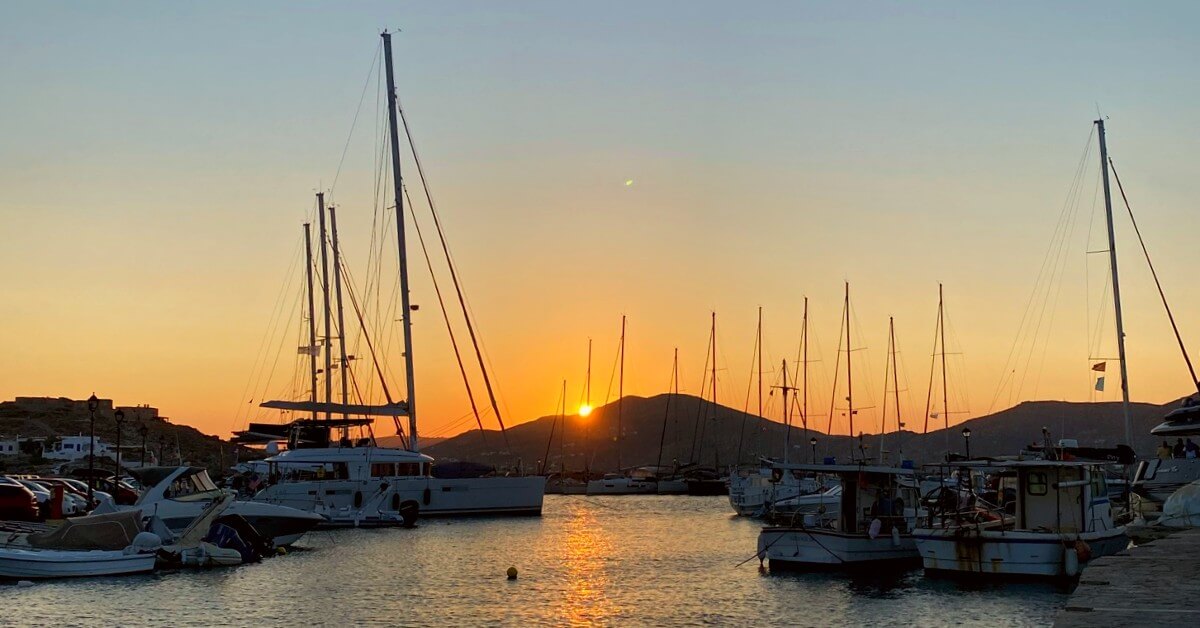 sunset in the port of naoussa paros over the hill, with boats in the sea