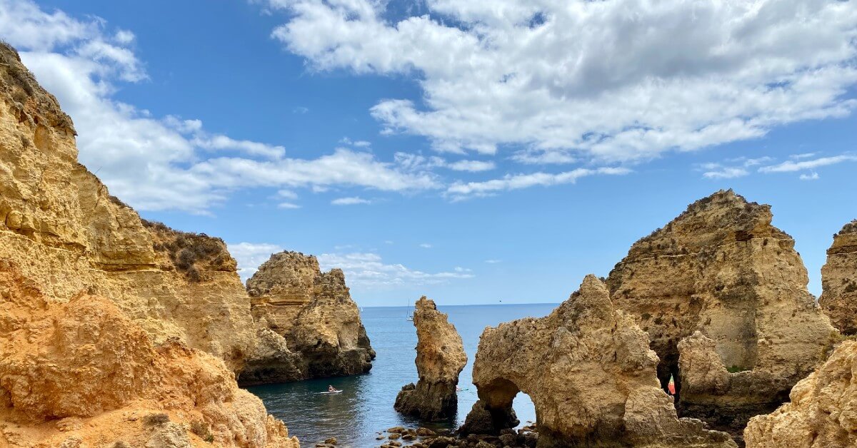 steep cliffs and unusual rock formations along the blue sea , with a person kayaking in lagos, portugal