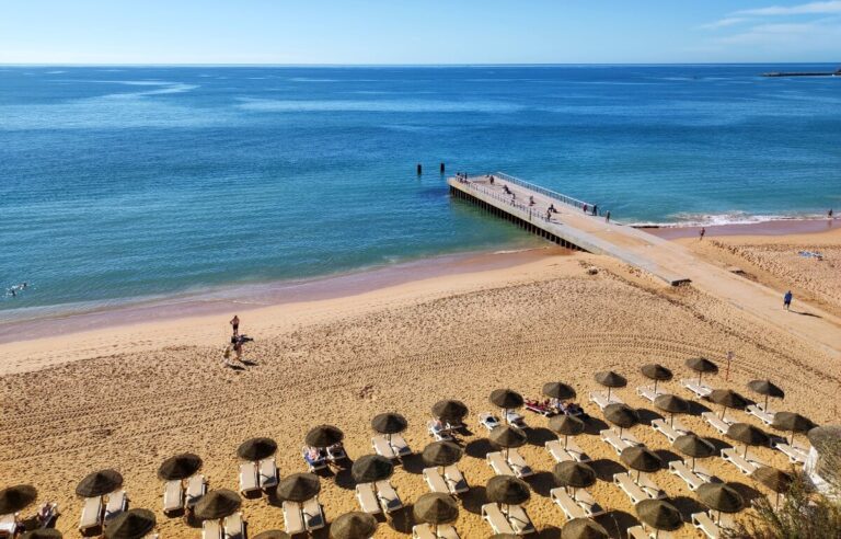 long sandy beach with several beach loungers and sun umbrellas in algarve portugal