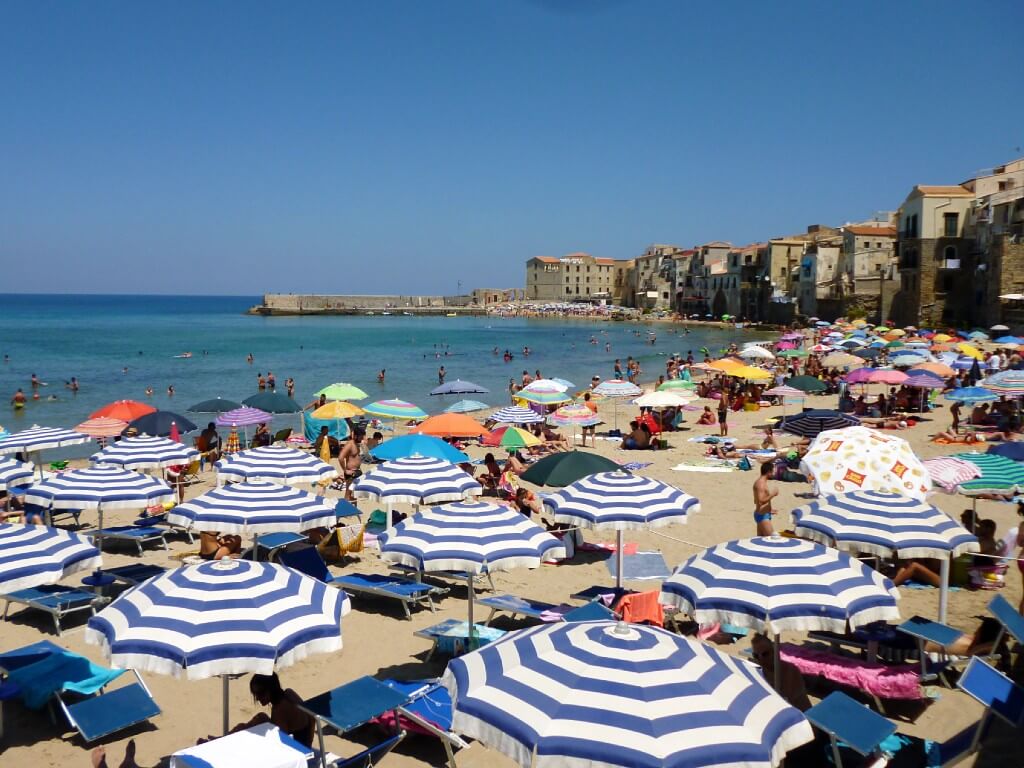 blue and white striped umbreallas on a beach in cefalu in sicily italy